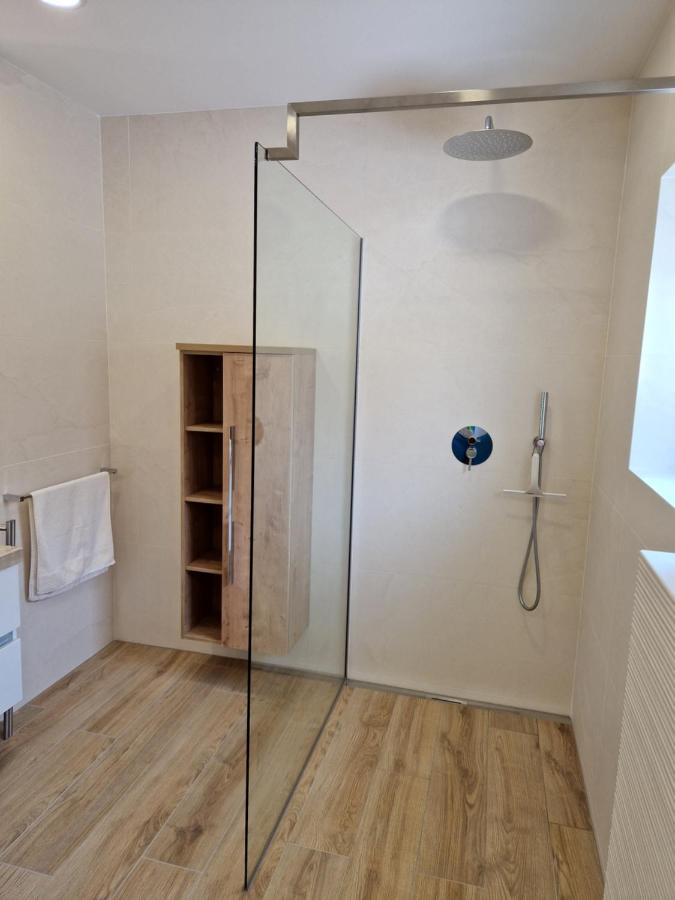 Minimalistična tuš kabina z veliko pršno glavo in naravnimi toni